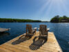 Cottage life - Sunrise on two empty Adirondack chairs sitting on a dock on a lake in Muskoka, Ontario Canada. The sun light create long shadows on the wooden pier.